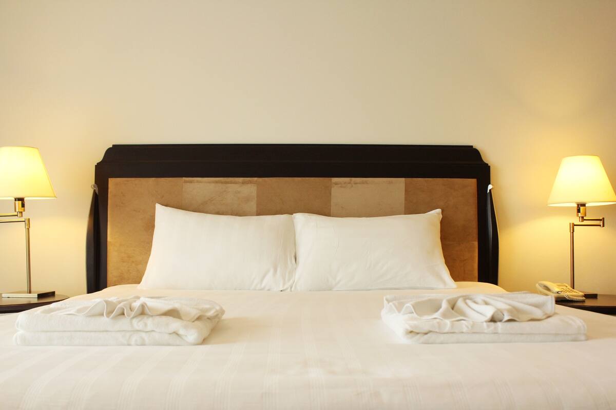 A neatly made bed with white linens and two pillows, flanked by two bedside lamps.