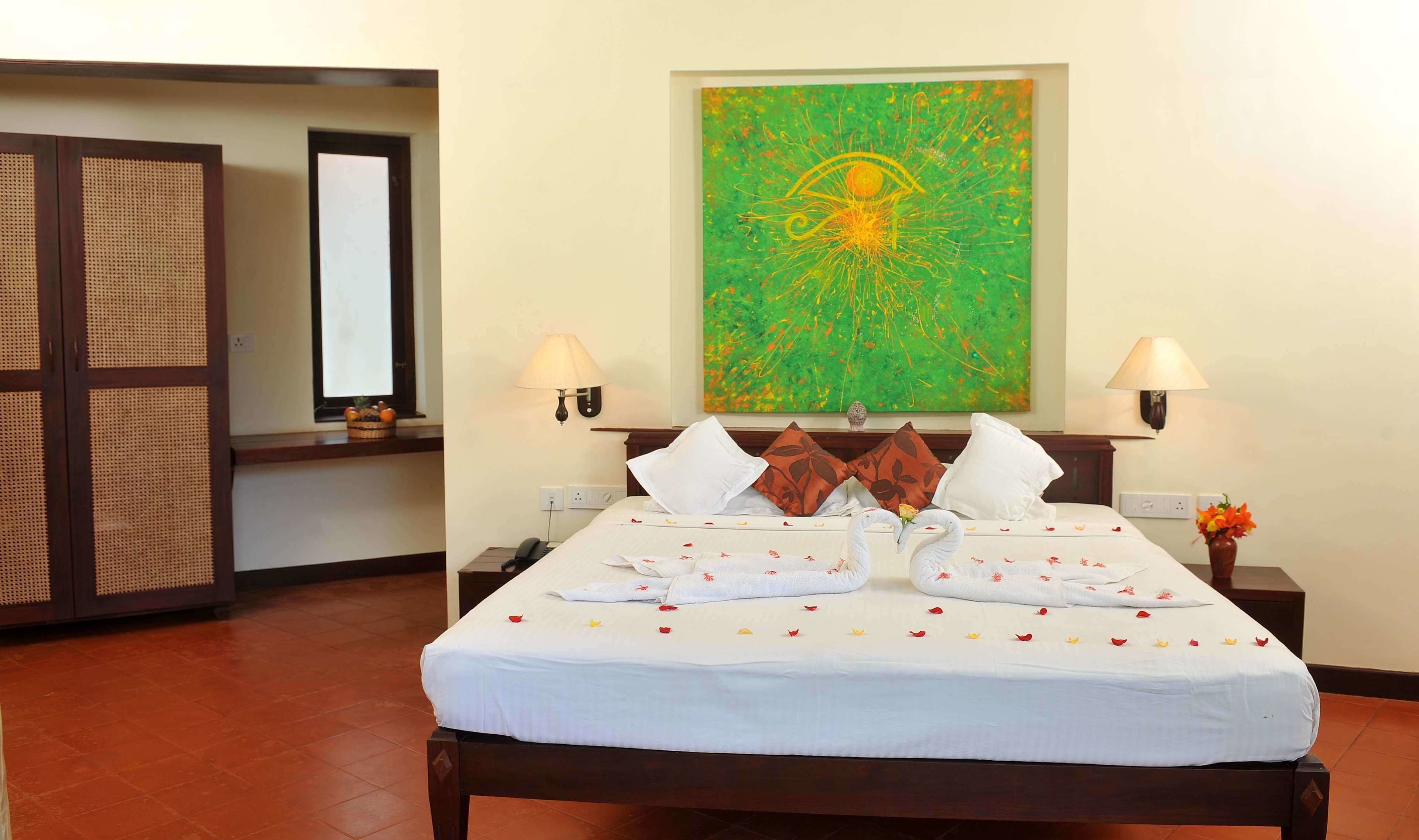A hotel room with a bed, two bedside lamps, a large abstract painting, and a wooden wardrobe.