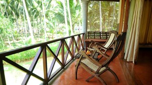 Un banco de madera con asiento y respaldo trenzados, ubicado sobre un suelo de baldosas con vistas a un jardín exuberante y altas palmeras.