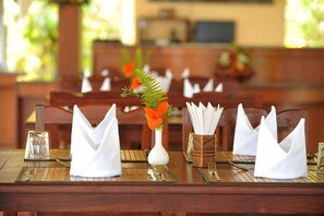 Una mesa de comedor dispuesta con servilletas blancas, un vaso de agua y un florero con flores anaranjadas.