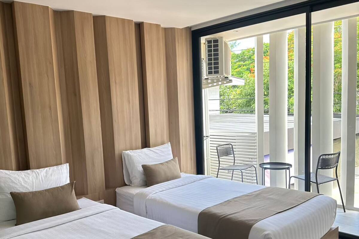 A hotel room with two beds, a large window, and a balcony with chairs.