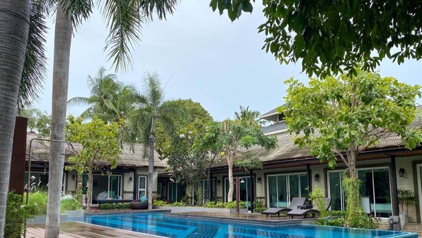 A swimming pool with tiled edges, surrounded by palm trees and a building with large windows. - Nirundorn Resort (Cha-am)