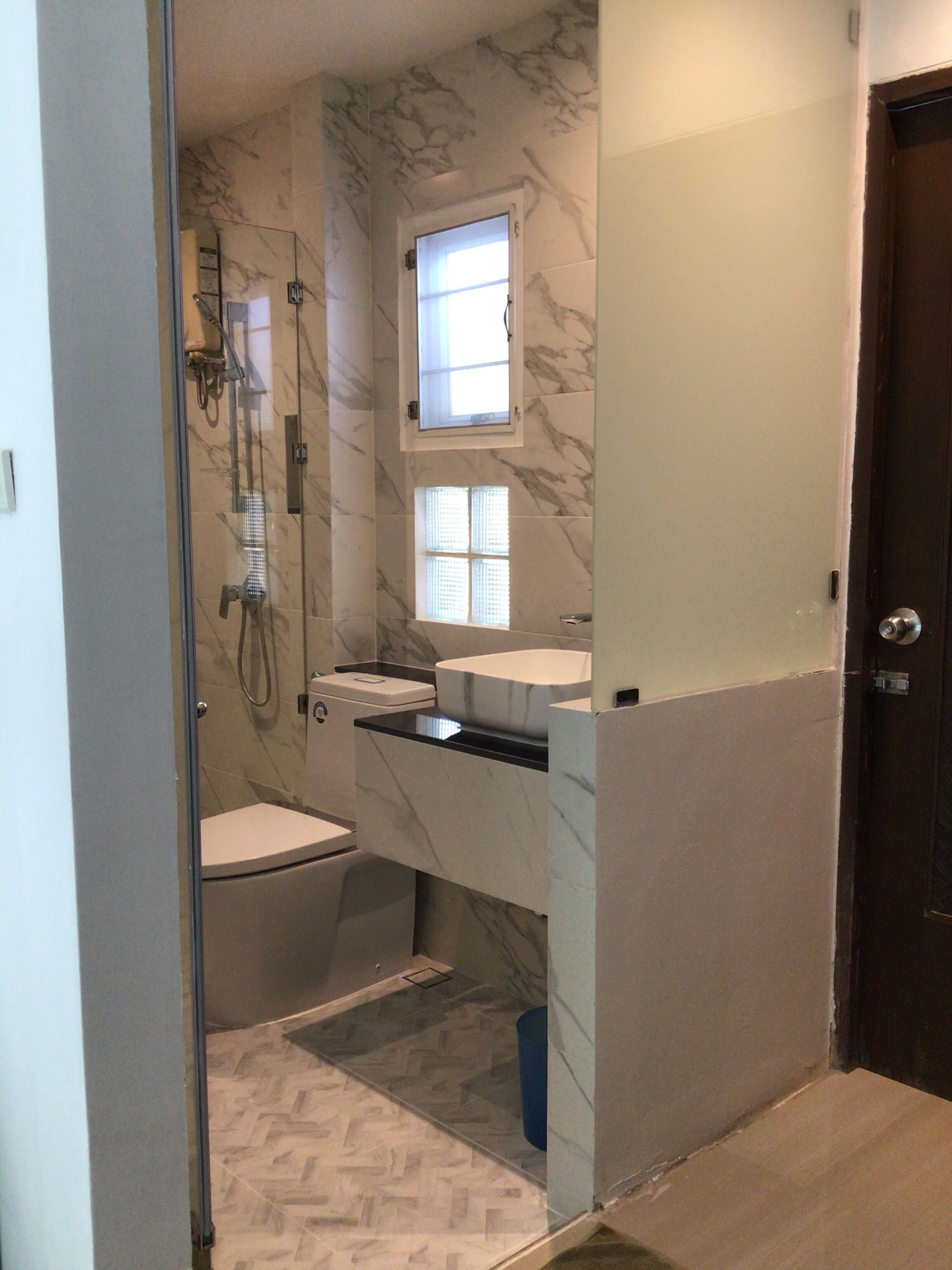 A bathroom with a glass-enclosed shower, a toilet, and a sink with a marble countertop.