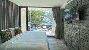 A modern hotel room with a large bed, a flat-screen TV mounted on the wall, and a view of the parking area through a sliding glass door. - Nirundorn Resort (Cha-am)