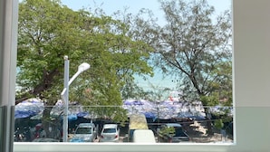 A view from a window with a metal railing, overlooking a parking area with cars and a beach with umbrellas. - Nirundorn Resort (Cha-am)