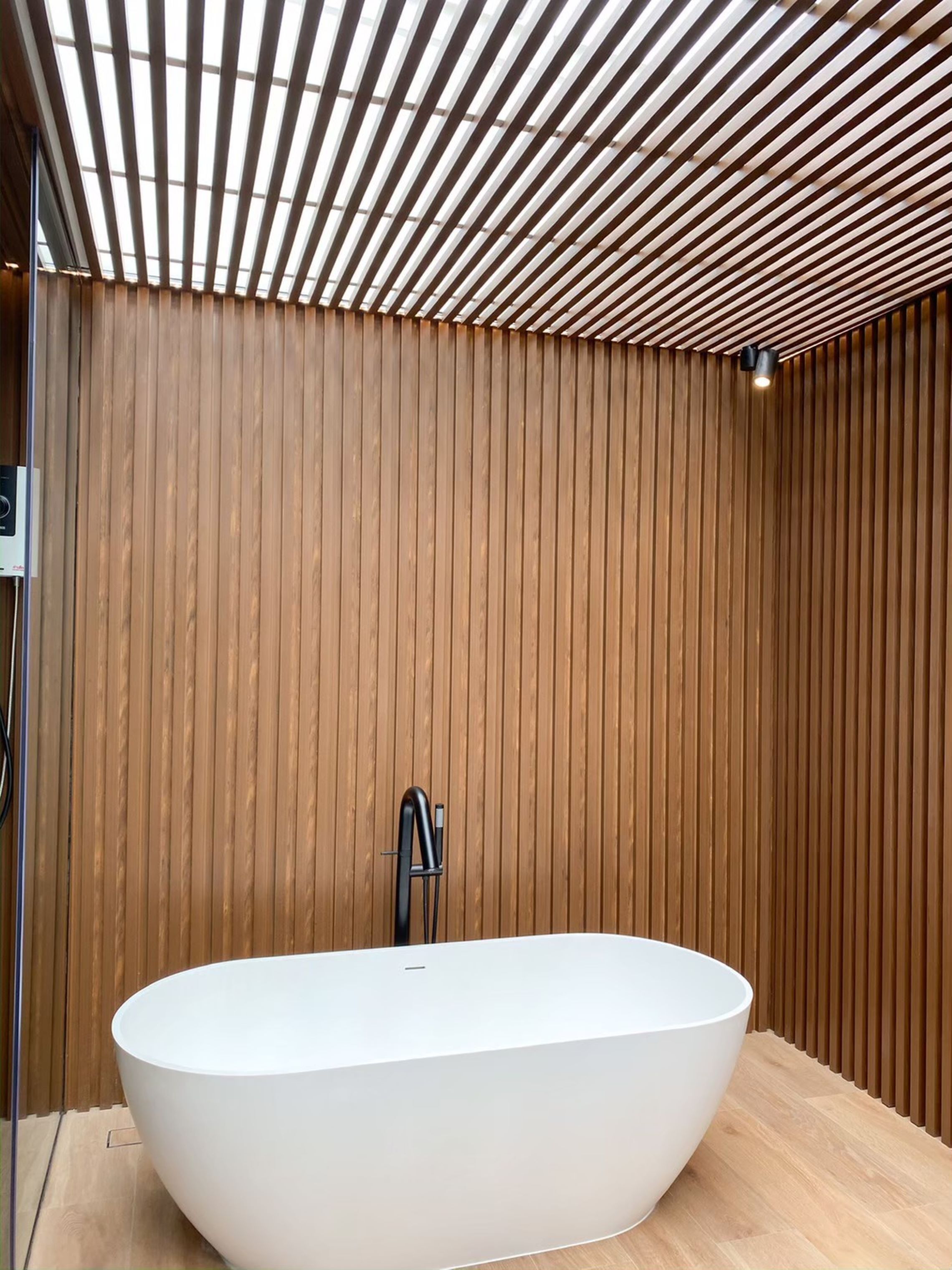 A modern bathroom with a freestanding bathtub, wooden panel walls, and a slatted ceiling.