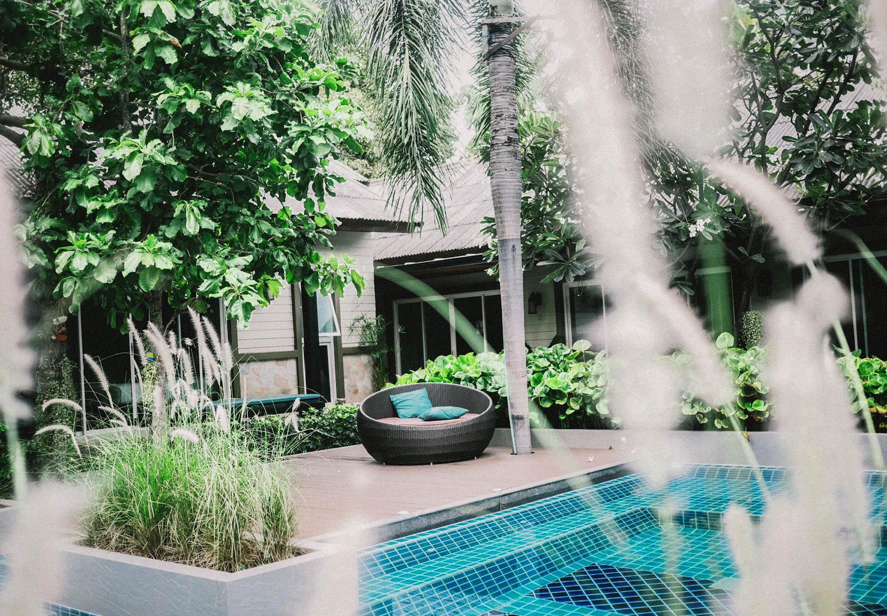 A swimming pool with a tiled edge, surrounded by lush greenery and a wicker chair.