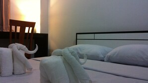 Una camera d'albergo con un letto, cuscini, una sedia e due asciugamani a forma di elefante.