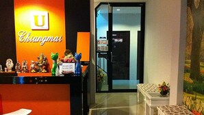 Un'area reception con il logo 'U' e la scritta 'Chiangmai', un banco con diversi oggetti, una porta in vetro che dà su una stanza e una panca con cuscino floreale.