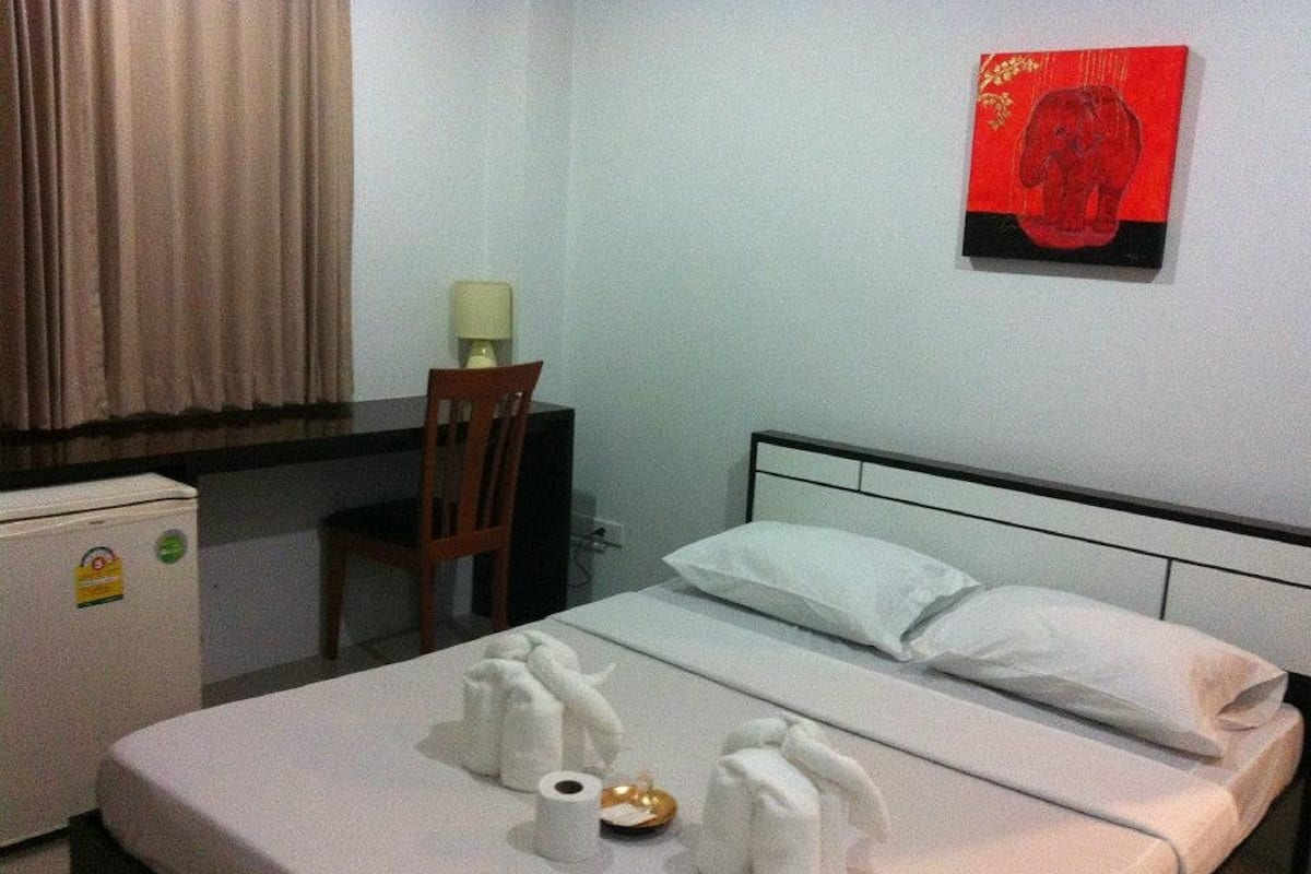 A hotel room with a bed, a desk, a chair, a small refrigerator, and a wall decoration.