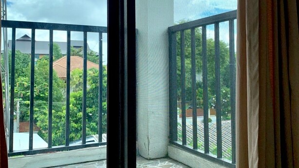 Un balcone con vista su una zona residenziale, una finestra con tenda e un pavimento piastrellato.