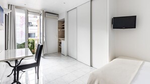 A modern hotel room with a bed, a TV mounted on the wall, a dining table with chairs, and a sliding door leading to a balcony. - Résidence Courcelle (Levallois-Perret)