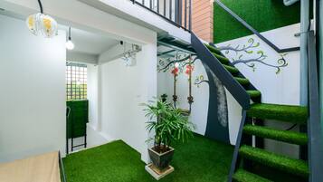 A modern interior with a staircase, artificial grass, a potted plant, and a hanging light fixture.