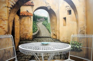 A courtyard with a stone pathway leading to a distant view, surrounded by arches and a white metal table with chairs. - Hapina Shel Michal (Mazkeret Batya)