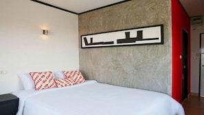 Ett modernt hotellrum med en stor säng, en röd accentvägg och ett inramat konstverk ovanför sängen.