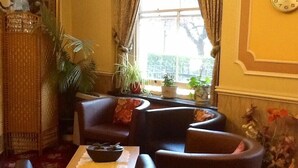 A cozy room with a large window, a wicker chair, a small table with a bowl, and a clock on the wall.