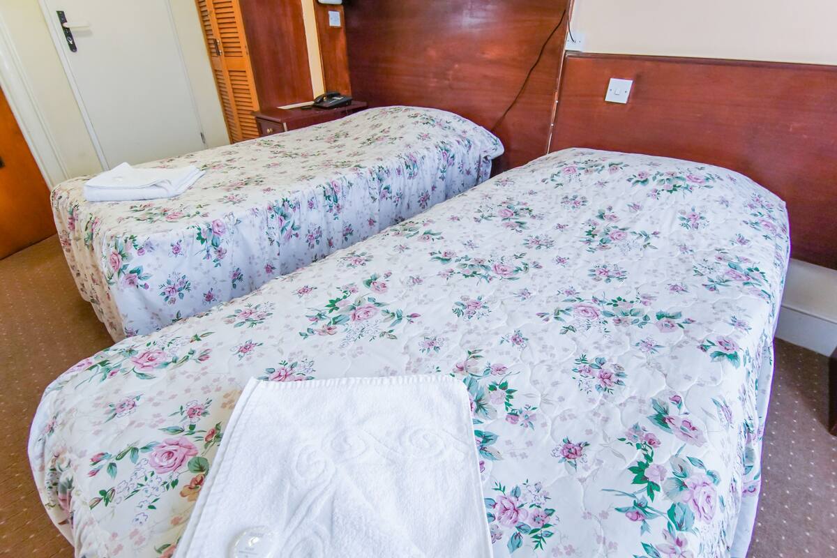 Two single beds with floral bedding, a wooden headboard, a white door, and a small bedside table with a phone.