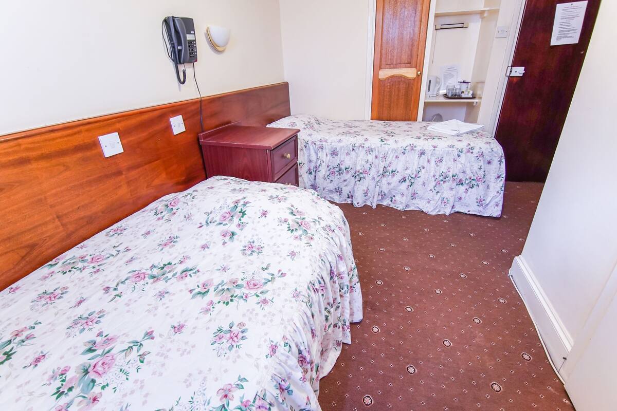 A hotel room with two beds, a wooden headboard, a bedside telephone, and a brown carpet.