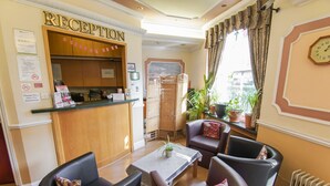 A reception area with a wooden counter, a seating area with two chairs and a table, and a window with curtains.