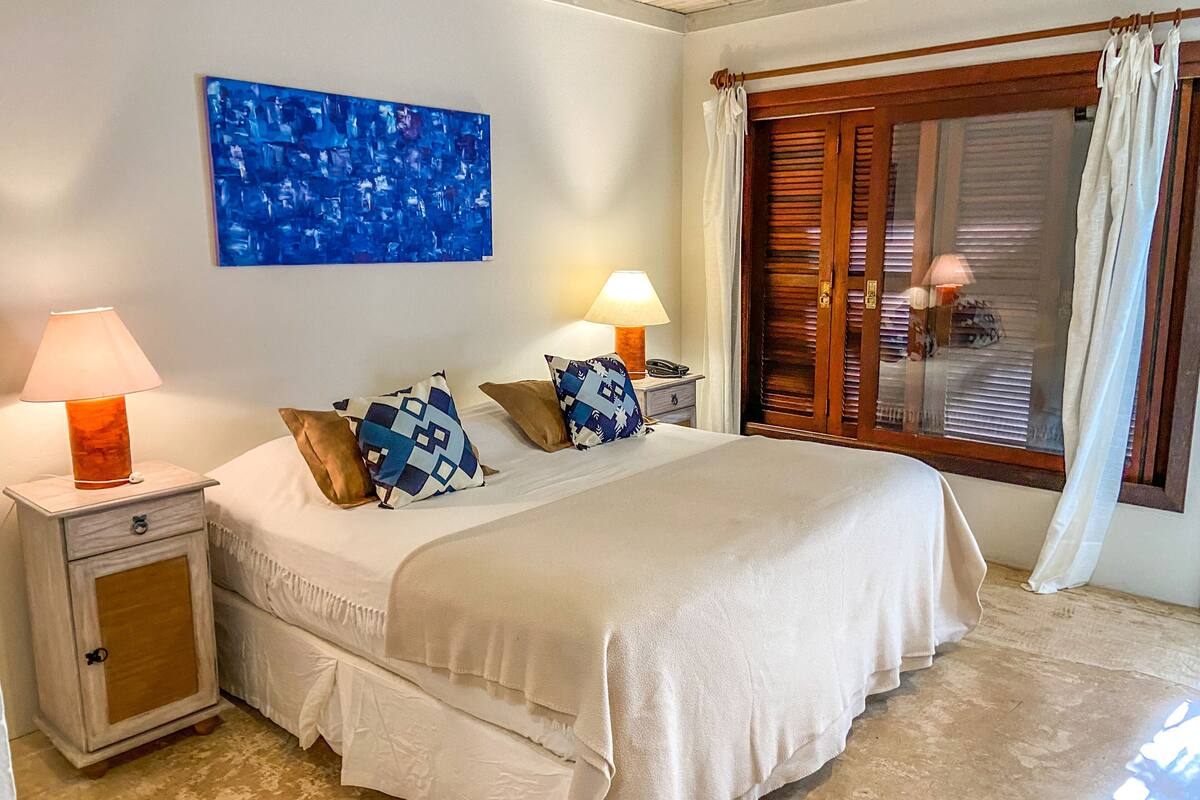 A neatly arranged bedroom with a bed, two bedside tables with lamps, a wooden door, and a window with curtains.