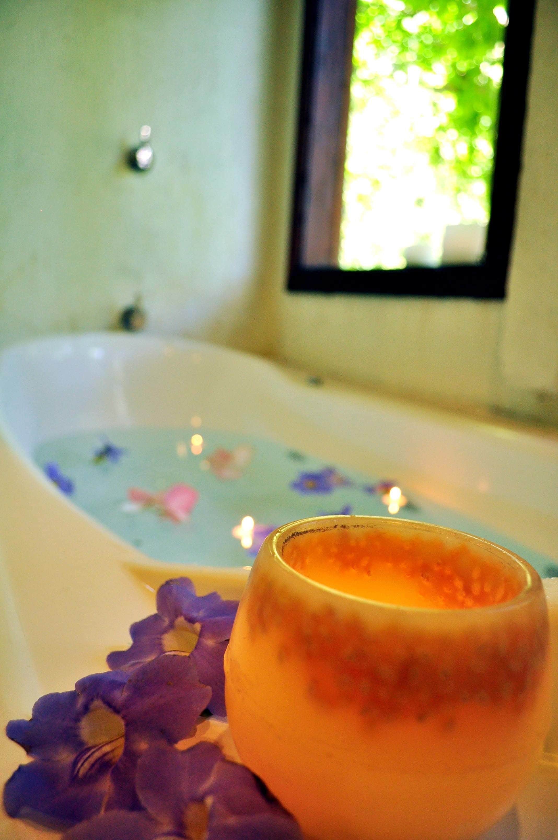 Una bañera con un tapete de baño floral y una vela en un recipiente de vidrio.