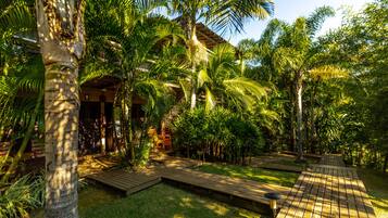 A tropical garden with a wooden deck, palm trees, and a building with a thatched roof.