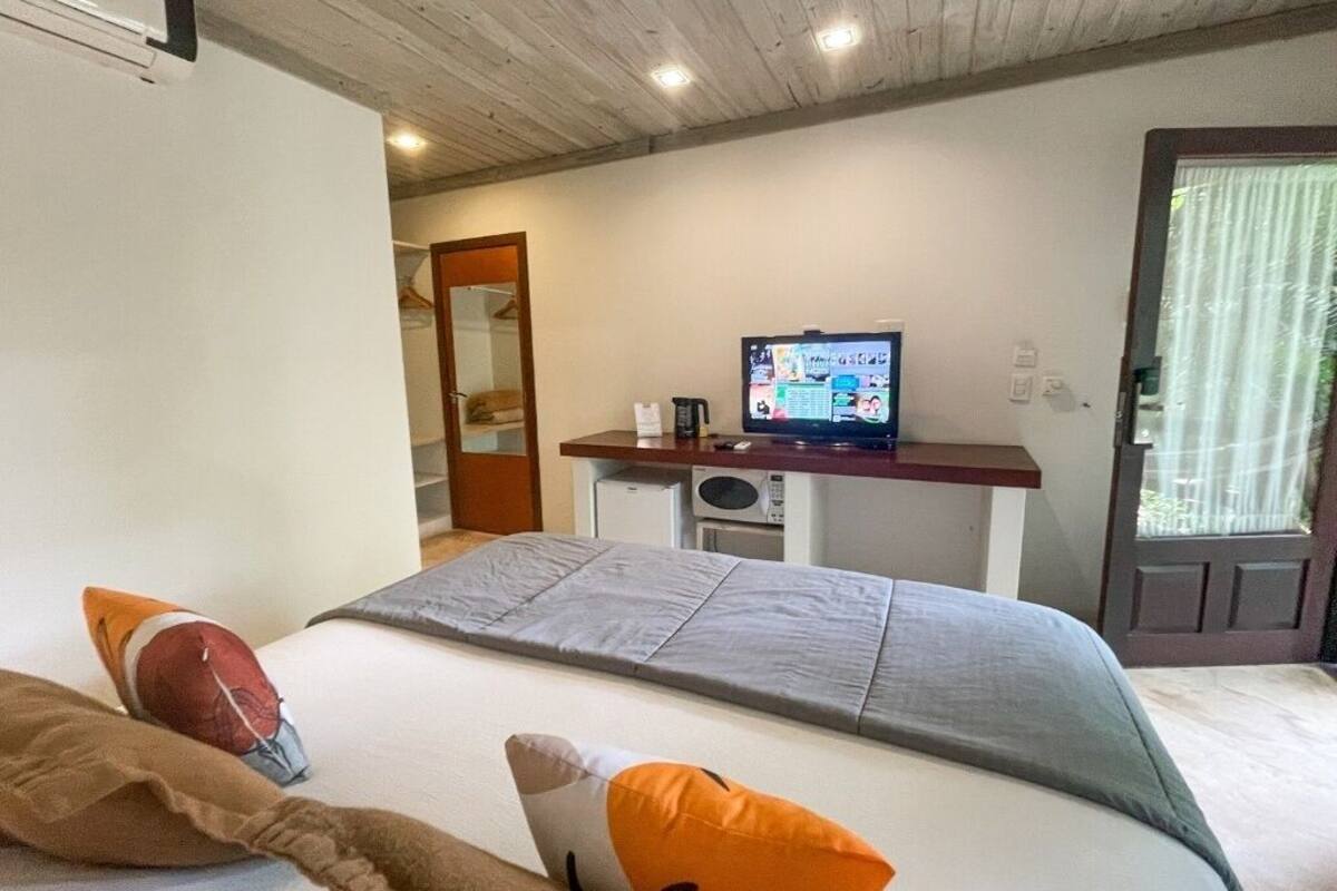 A hotel room with a bed, pillows, a television, a microwave, and a door.
