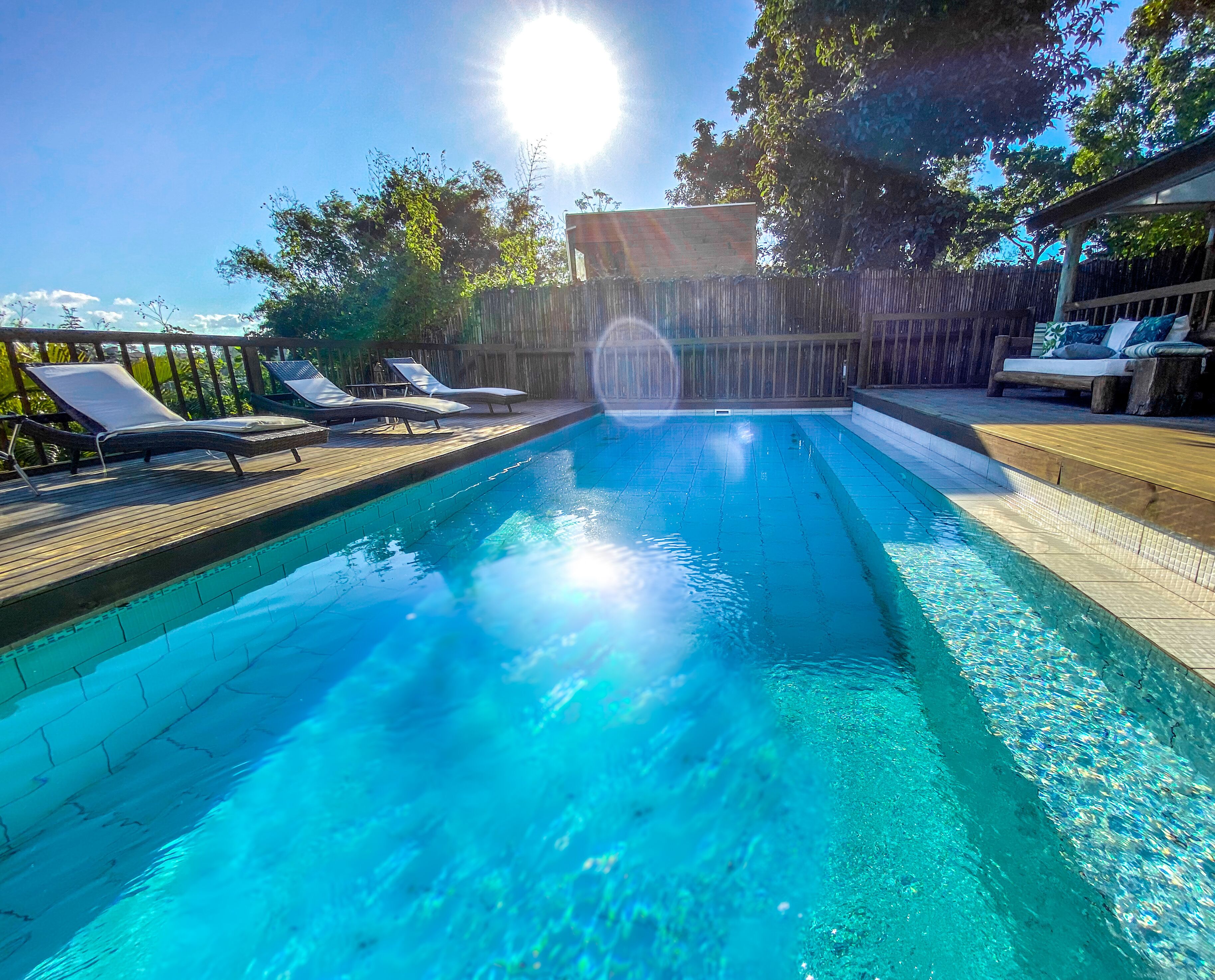 A clear blue pool with lounge chairs and a wooden deck.
