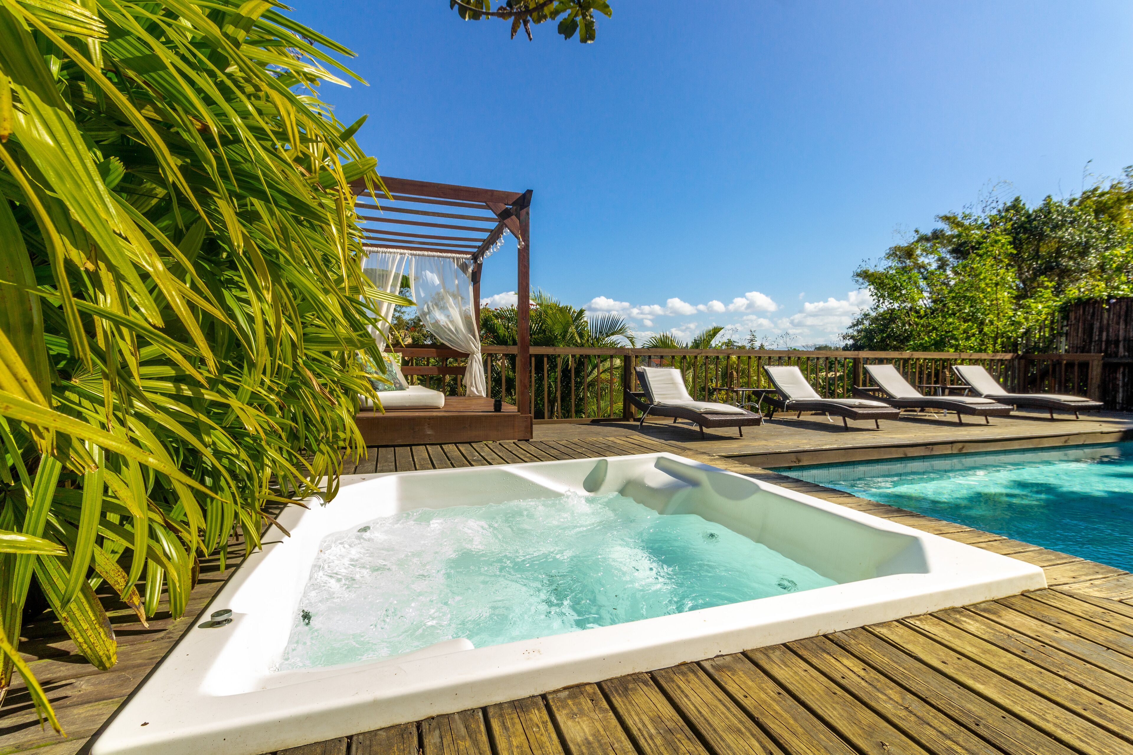 Una terraza de madera con un jacuzzi, sillones de descanso y una pérgola con toldo.