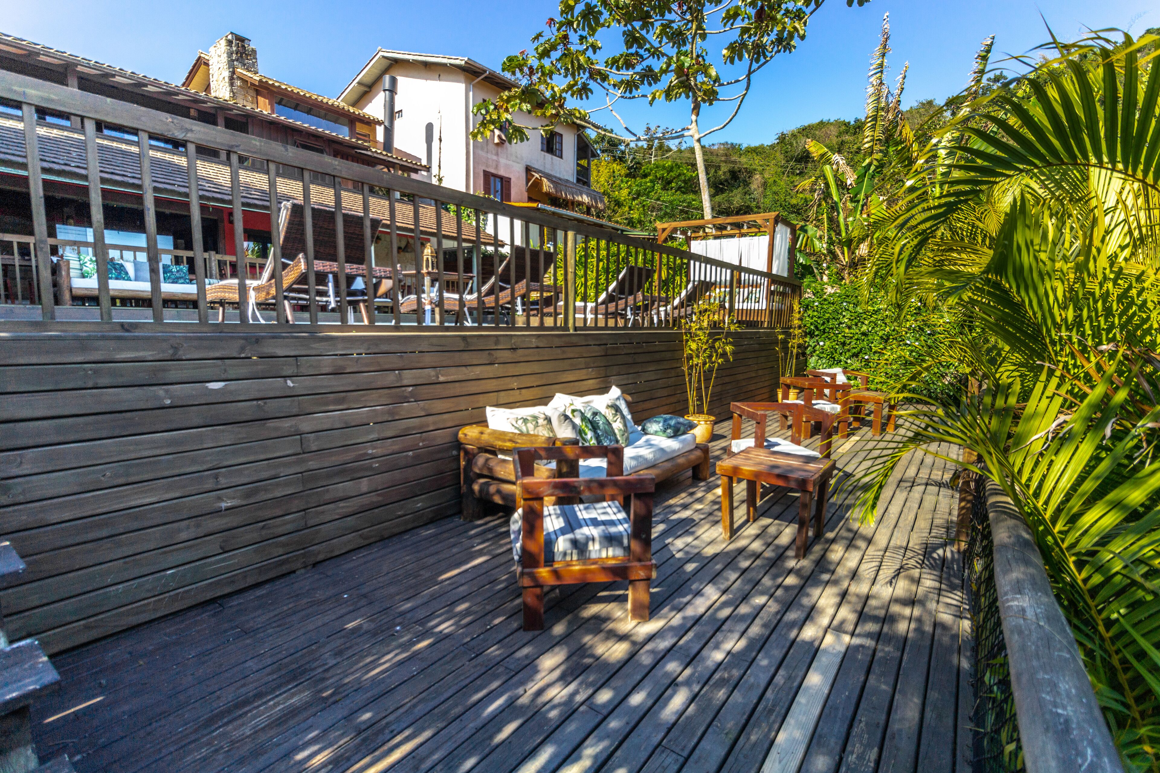 A wooden deck with outdoor seating, including a sofa and chairs, surrounded by lush greenery.