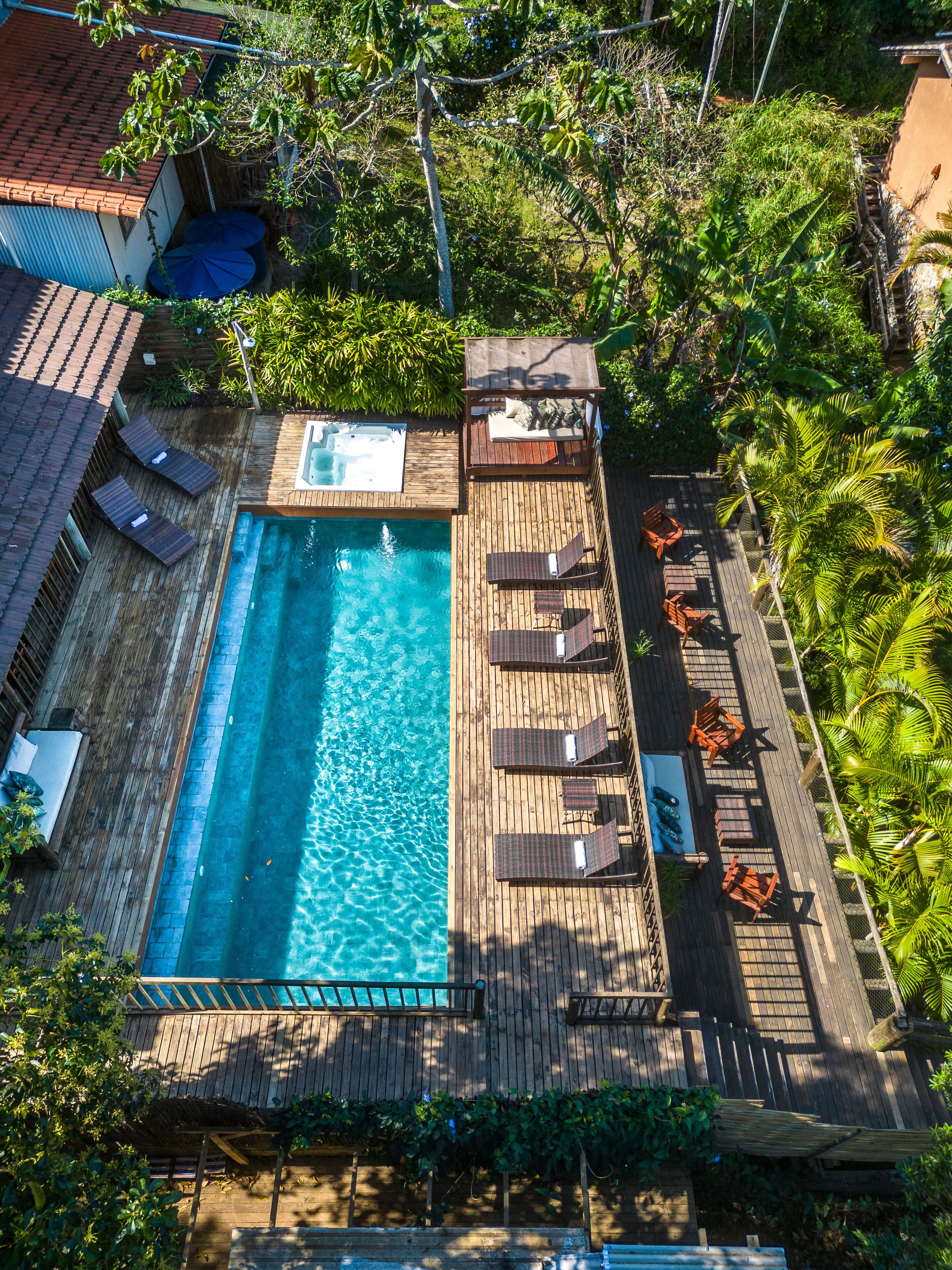 A wooden deck with a swimming pool, lounge chairs, and a hot tub.