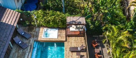 A wooden deck with a swimming pool, lounge chairs, and a hot tub.