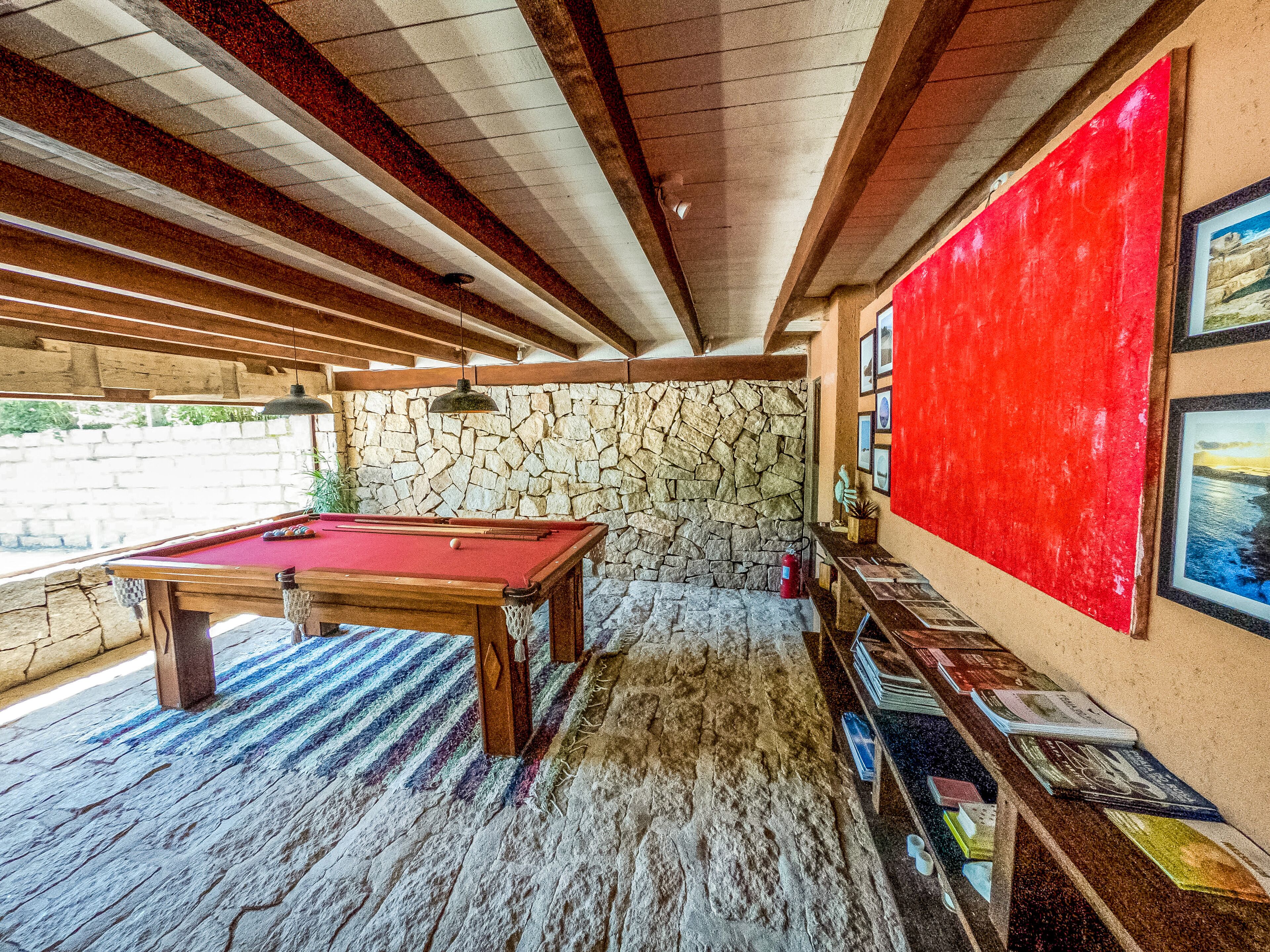 A pool table with a red felt surface, a stone wall, and a red accent wall with framed pictures.