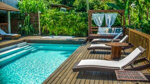 A wooden deck with a pool, lounge chairs, and a canopy. - Pousada Morada da Praia do Rosa (Imbituba)