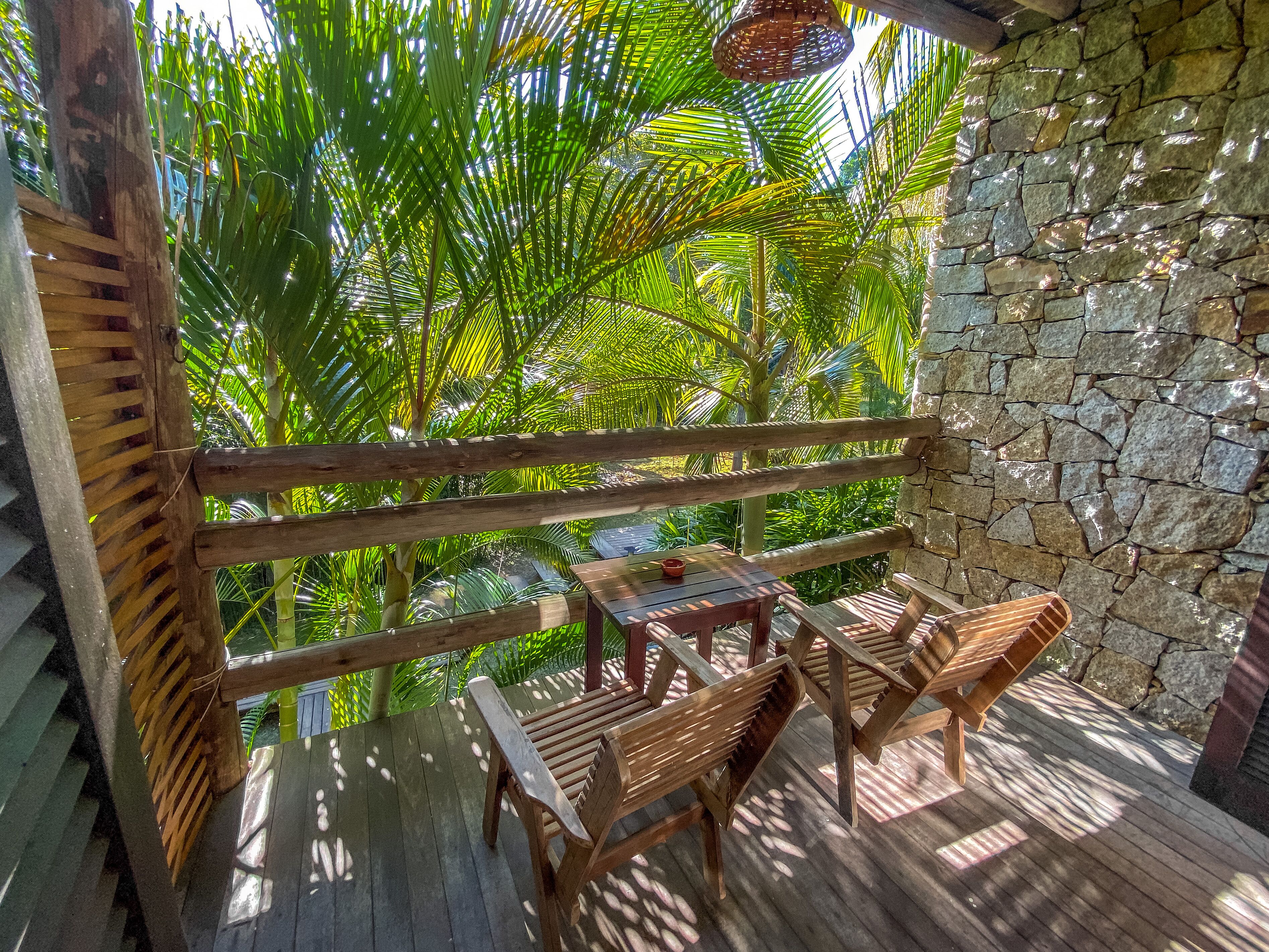 A wooden deck with a stone wall, a hanging basket, and a table with chairs.