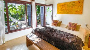 A bedroom with a bed, a bench, a window with shutters, and a painting on the wall. - Pousada Morada da Praia do Rosa (Imbituba)