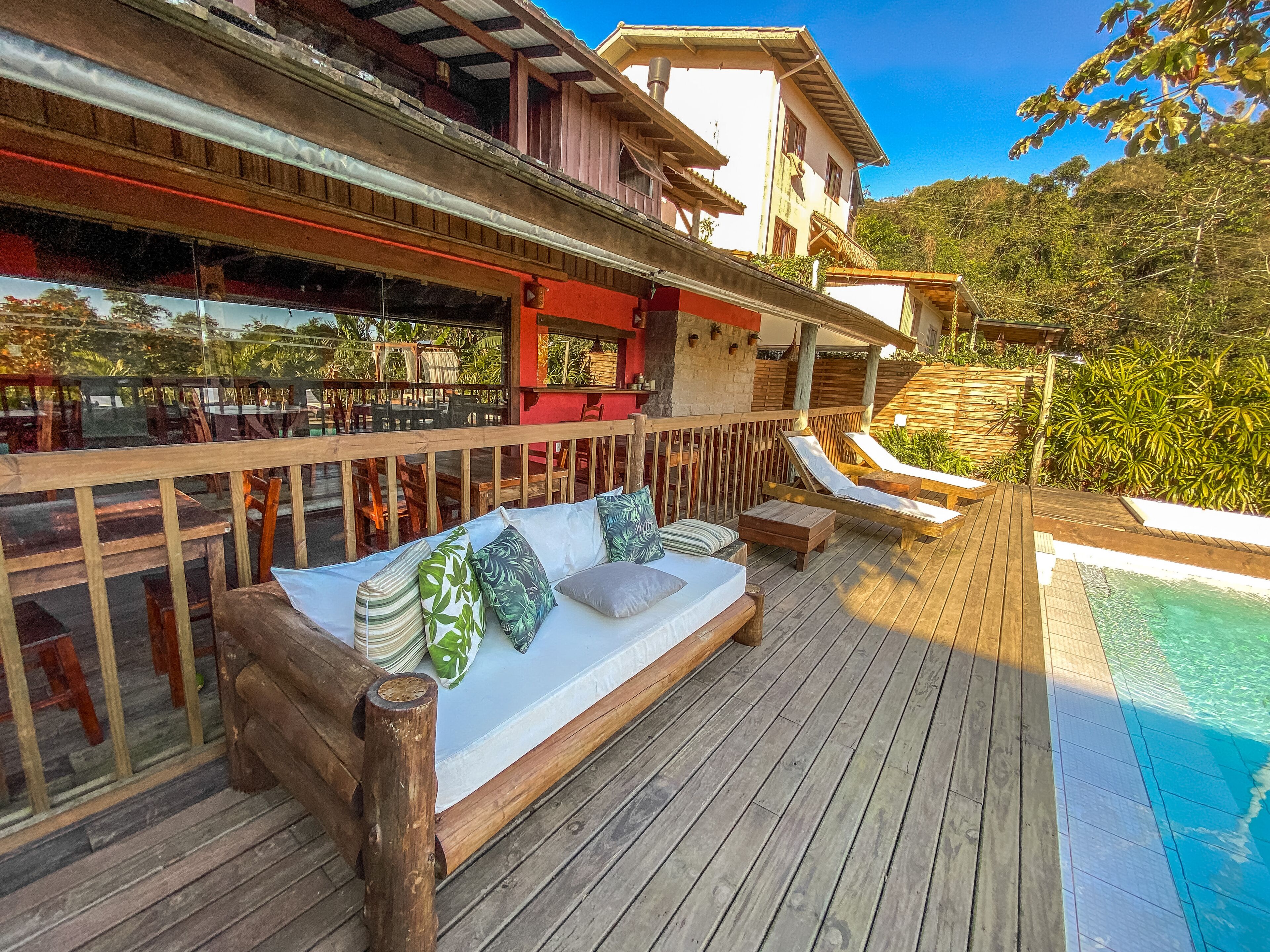 Una terraza de madera con piscina, asientos al aire libre y vistas al entorno verde.
