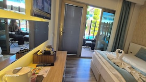 Hotelkamer met een bed, een bureau met een afstandsbediening, een klein tafeltje met een waterfles en uitzicht op buiten.