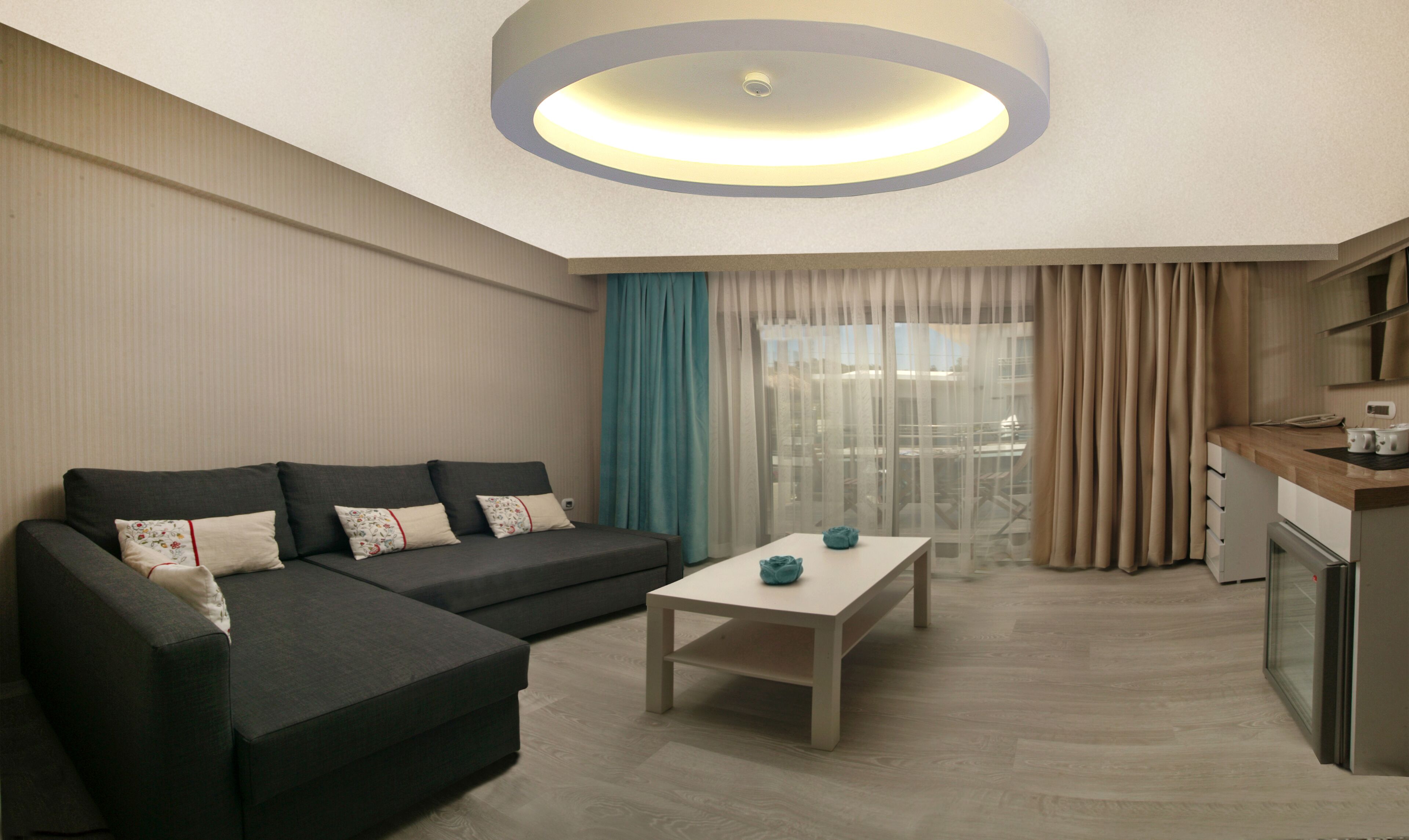 A modern living room with a sectional sofa, a small coffee table, and a kitchen area with a refrigerator.