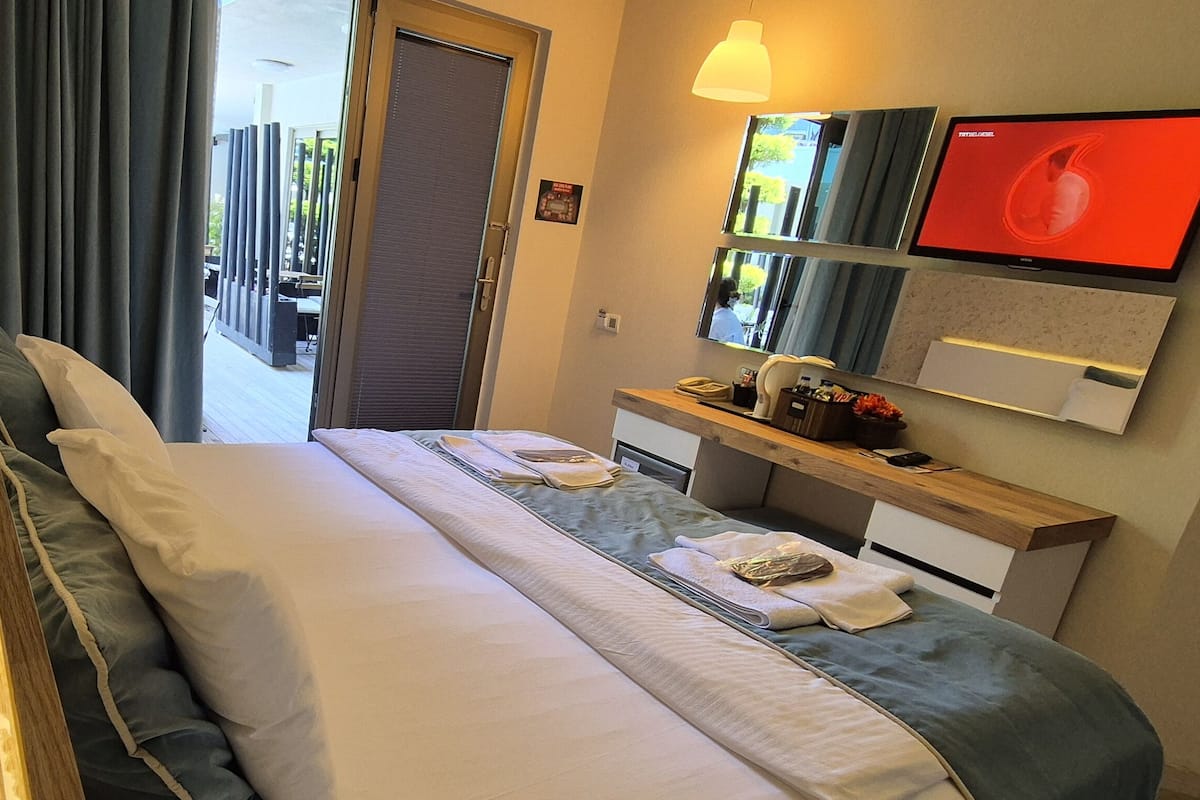Une chambre d’hôtel avec un lit, une table de chevet avec une lampe, un miroir et un téléviseur.