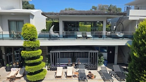 Een modern gebouw met een terras op het dak, buitenmeubels en een verzorgde tuin.
