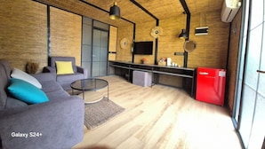 Een moderne woonkamer met een Galaxy S24+ op een bank, een rode koelkast, en een keuken met een televisie en decoratieve objecten.