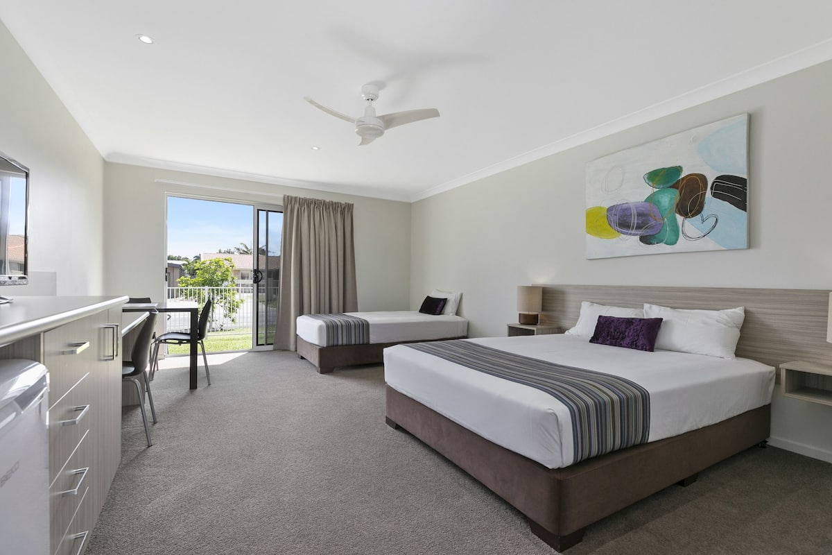 Quarto de hotel com duas camas, uma escrivaninha e varanda.