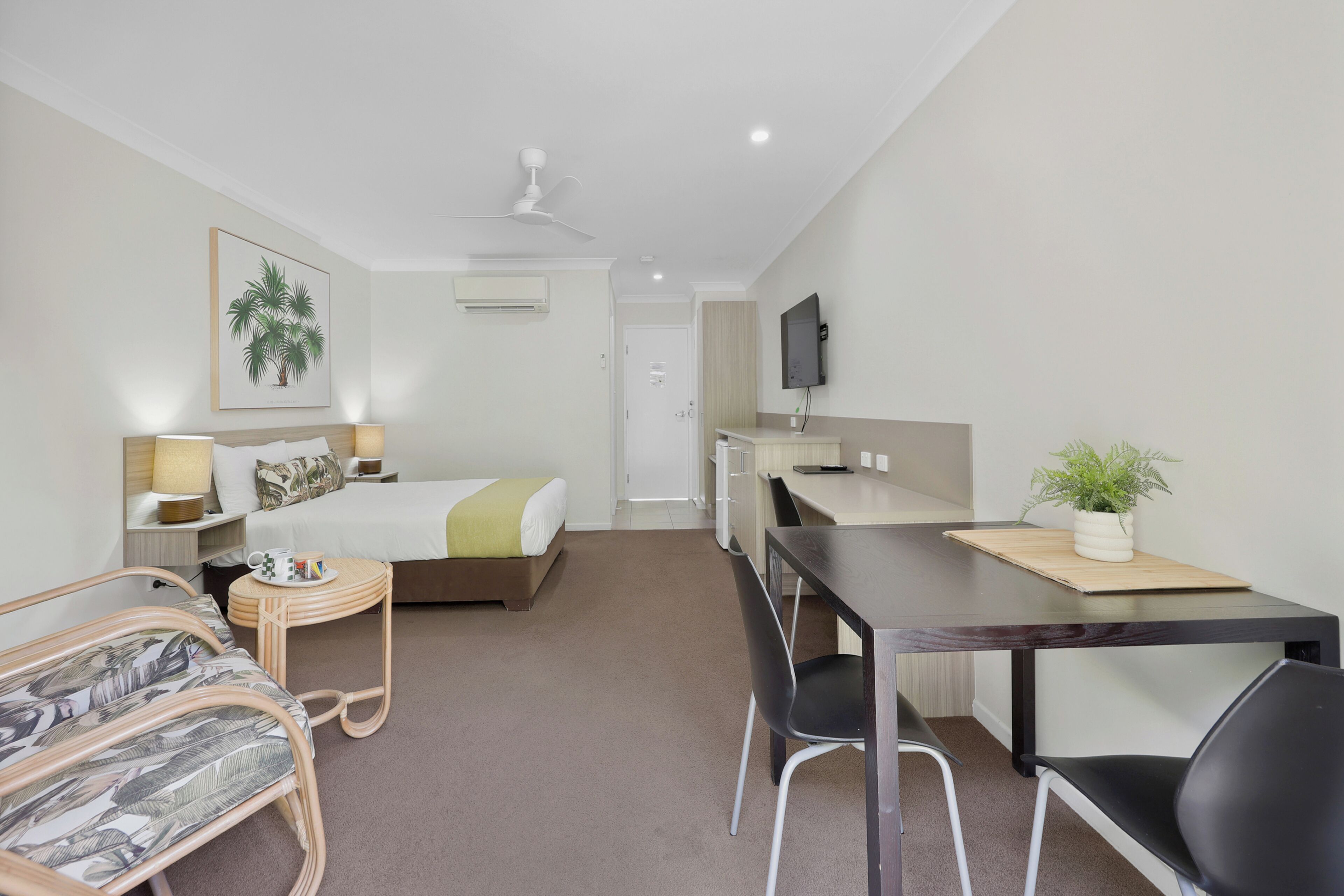 Une chambre d’hôtel équipée d’un lit, d’un bureau, d’une chaise, d’une petite table, d’un téléviseur et d’une plante.