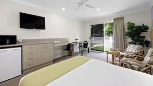 Habitación de hotel con cama, escritorio, televisor, ventilador de techo y vistas al exterior.