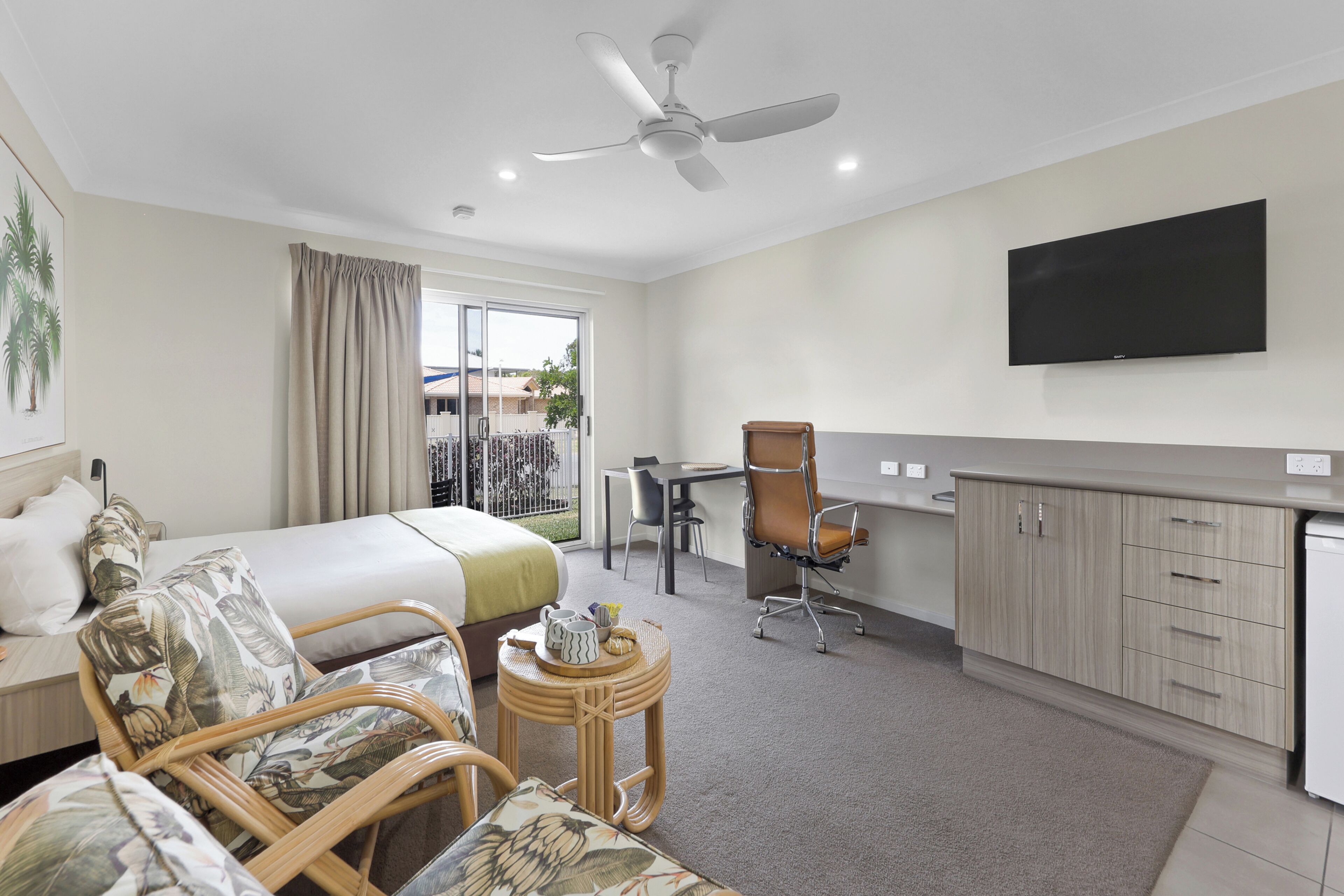 Una habitación de hotel con cama, escritorio, silla, televisión y balcón con vistas.