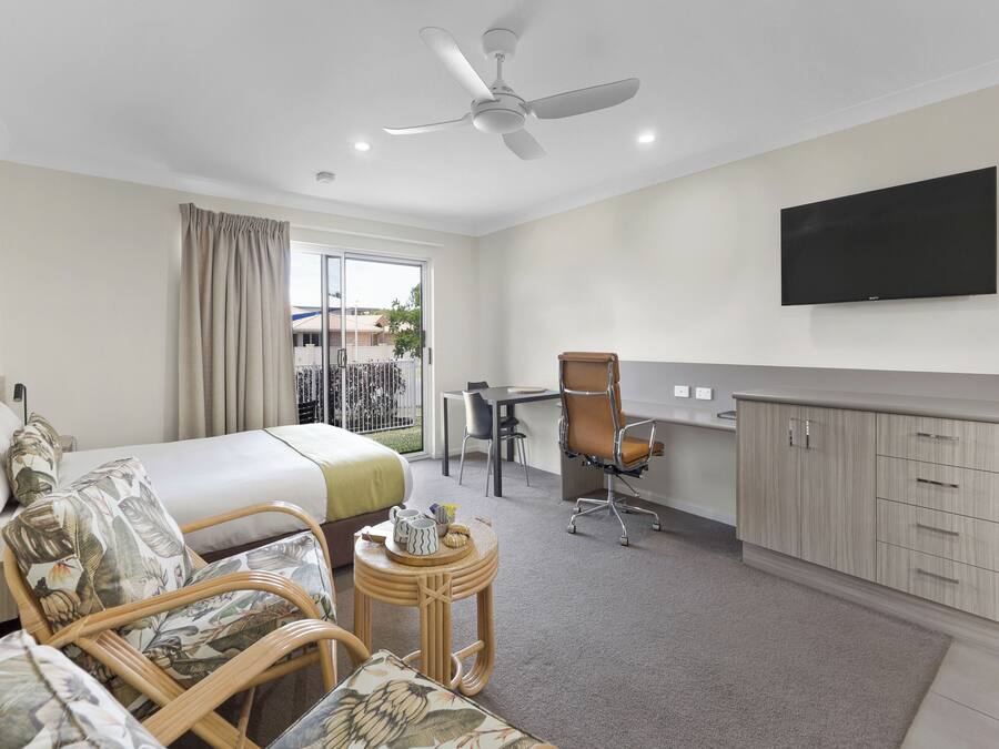 Quarto de hotel com cama, escrivaninha, cadeira, televisão e varanda com vista.