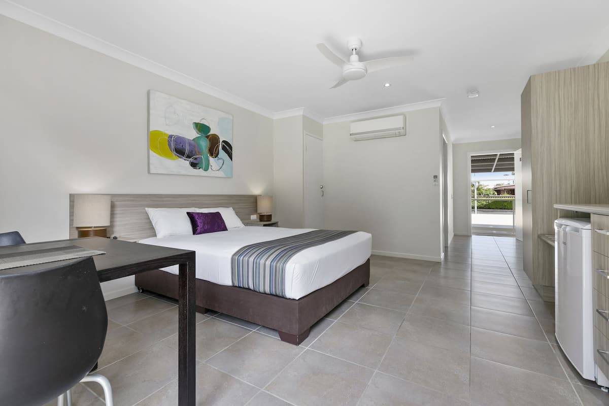 Quarto de hotel moderno com cama, escrivaninha, ventoinha no teto e vista para o exterior.