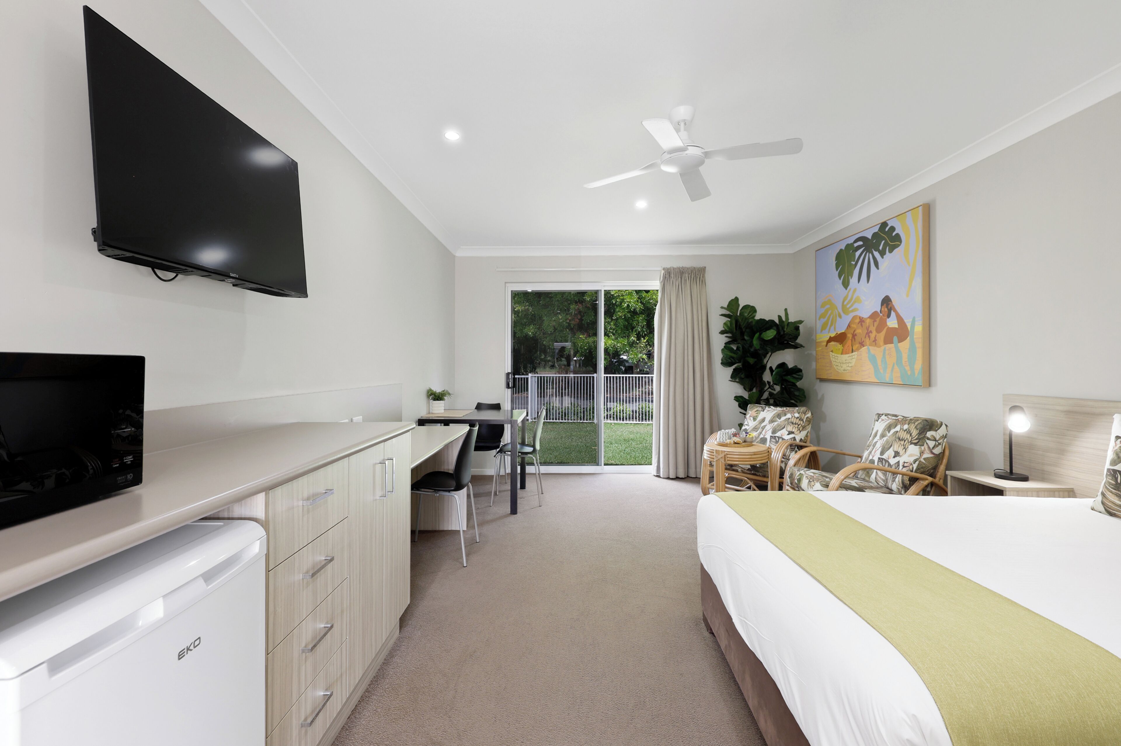 A hotel room with a bed, a desk, a television, a ceiling fan, and a sliding glass door to the outside.