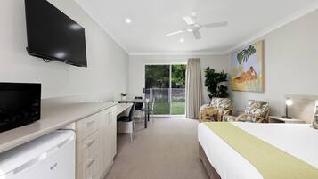 A hotel room with a bed, a desk, a television, a ceiling fan, and a sliding glass door to the outside.